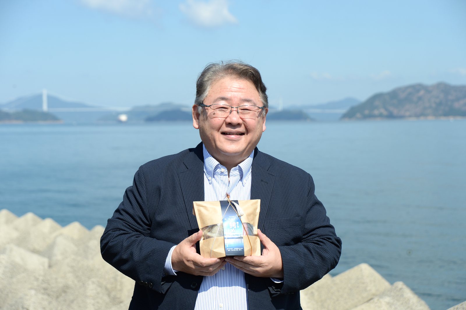 瀬戸内海を背に、瀬戸内鯛めしを手にする愛媛海産 代表取締役の大塚康仁さん