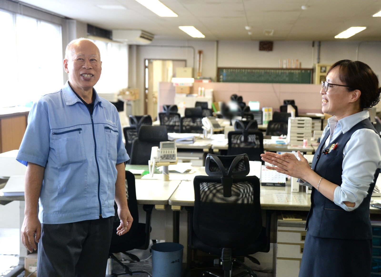 撮影が行われた事務所で、映画のシーンを再現する砂田和彦さんと武田江利子さん